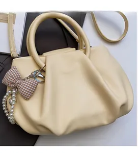 Detail view of the soft pleated texture and decorative pearl charm on the beige handbag