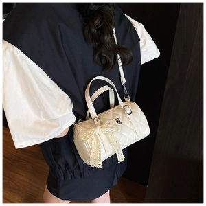 Close-up of a white quilted cylinder bag with a lace bow and silver hardware detail