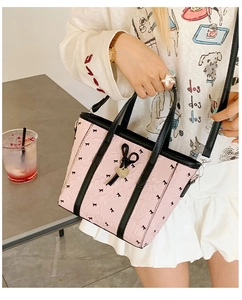 Gros plan d'un sac cabas rose avec motifs nœuds noirs et pendentif doré en cœur