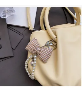 Detail of a brown plaid bow and pearl chain pendant on a beige leather handbag