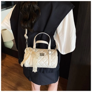 Close-up of white quilted cylinder bag with lace bow and elegant glossy finish