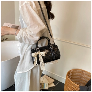 Detail view of black quilted cylinder bag with cream lace bow and silver metal buckle
