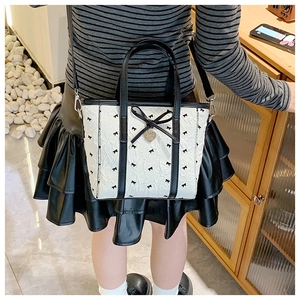 Détail du cabas montrant les motifs de nœuds et le pendentif cœur doré sur un mannequin