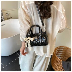 Detail of black quilted patent leather Boston bag with silver lock and lace bow charm