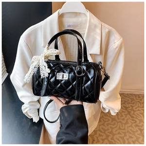 Detail of black quilted cylinder bag featuring a silver square lock and white lace bow