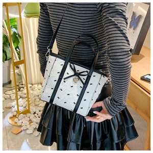 Vue détaillée d'un sac cabas blanc avec motifs nœuds noirs et pendentif en cœur