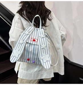 Close-up of cute long rabbit ears with white stars on a blue striped fashion backpack