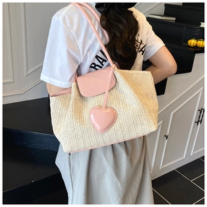 Detail of straw woven tote with pink leather trim and heart charm on modern model