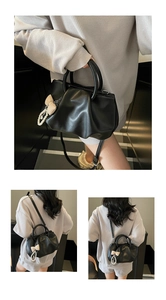 Detail of black pleated cloud bag with round handle and pearl bow charm accessory
