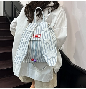 Close-up of cute rabbit ears and white plush star detail on blue striped canvas backpack