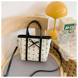 Détail du sac cabas crème avec imprimés nœuds noirs, nœud en cuir 3D et pendentif en cœur
