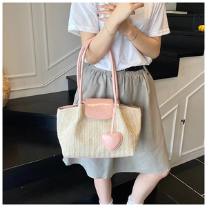Detail of woven straw tote with pink leather handles and heart charm accessory