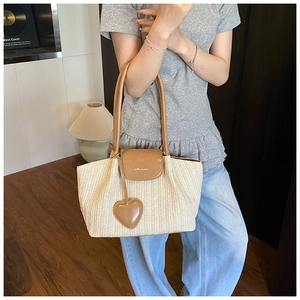 Detail of woven straw tote bag with brown leather handles and heart pendant on shoulder