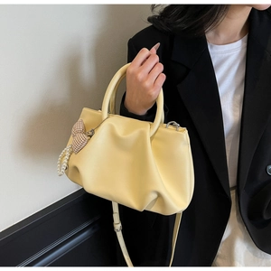 Detail of light yellow pleated cloud bag with pearl and checkered bow charm accessories