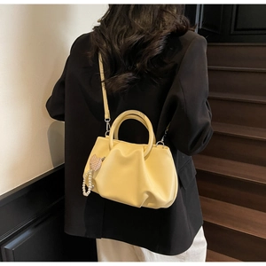 Detail view of yellow pleated cloud bag with soft leather texture and pearl heart charm