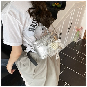 Detail of silver metallic box bag with pearl charms and lace bow on a textured surface