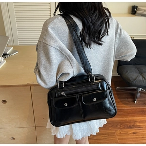 Detail view of black glossy shoulder bag with two snap pockets and silver metal buckles