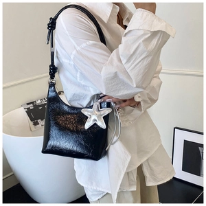 Détail du sac sous le bras en cuir verni noir avec breloque étoile argentée et bandoulière
