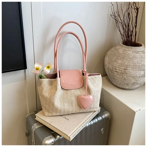Detail of woven straw tote bag with pink leather handles and heart charm on suitcase