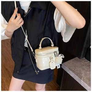 Close-up of cream glossy leather handbag with pearl charm and slender shoulder strap