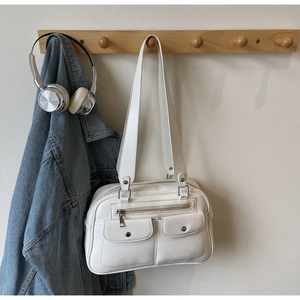 White vintage faux leather baguette bag with metal rivet pockets shown on a wooden rack