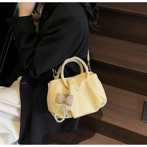 Detail of pleated cloud bag in pale yellow featuring round handles and pearl decor