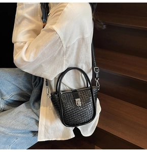 Détail d'un sac seau en cuir tressé noir avec fermoir argenté porté par un mannequin