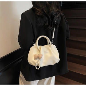 Detail of a creamy white pleated cloud bag with pearl bow charm on a black blazer background