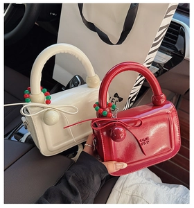 Dettaglio di mini borse lucide con manici rotondi e ciondoli sferici in bianco e rosso