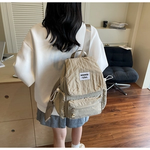 Detail view of light khaki nylon backpack with side drawstring pockets and logo patch