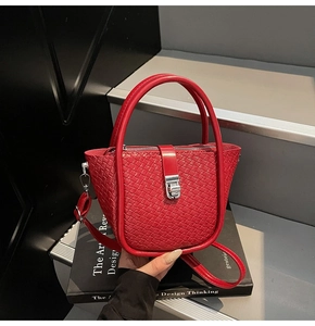 Détail du sac seau rouge tressé montrant la texture, le fermoir rotatif et la bandoulière