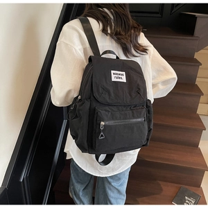 Casual black drawstring backpack with front pocket and white logo tag on stairs