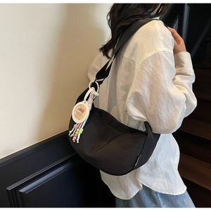 Détail du sac croissant en nylon noir avec bandoulière large et pendentif décoratif