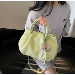 Detail of light green pleated handbag featuring chic bow charm and long strap