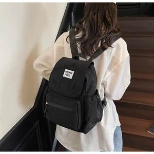 Detail of black nylon backpack featuring drawstring flap closure and white woven text label