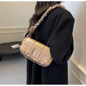 Détail du sac à bandoulière plissé beige avec bandoulière à volants sur un manteau noir