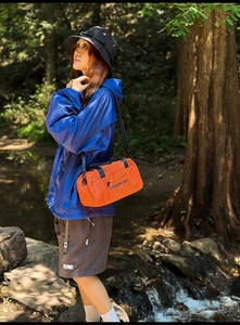 Outdoor model wearing a bright orange nylon crossbody bag with blue athletic jacket