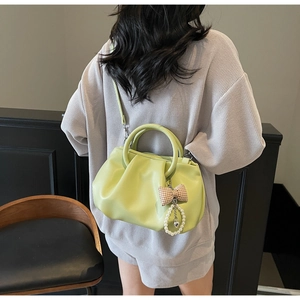 Detail of light green pleated soft leather tote with pearl bow charm worn by model