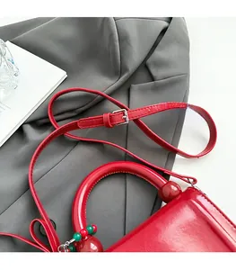 Dettaglio della borsa rossa lucida con tracolla regolabile e ciondolo con perline