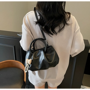Detail of black pleated cloud bag with soft leather texture and pearl ribbon charm