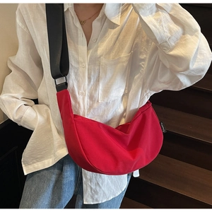 Détail du sac croissant rouge avec large bandoulière noire réglable porté par un mannequin