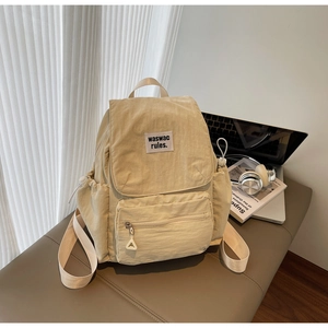 Detail of beige nylon backpack with drawstring flap and front patch on a stylish bench