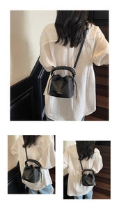 Detail of black litchi grain bucket bag with woven handle and gold brand lettering
