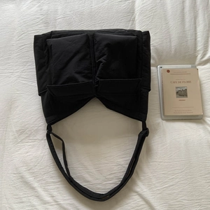 Detail of black quilted nylon tote bag featuring large symmetrical pockets and wide shoulder straps