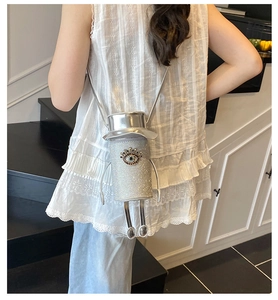 Detail view of the silver sequin hat-shaped crossbody bag worn by a model on stairs