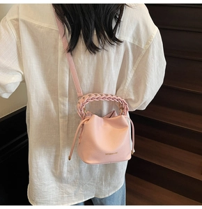Close-up of a light pink bucket bag with woven handle worn by a model on stairs