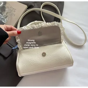 Detail der weißen Schleifenhandtasche mit Magnetverschluss und Spitzenbesatz am Rand