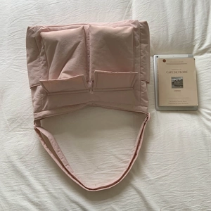 Flat lay of a pink quilted puffer tote bag with double pockets on a white bed sheet