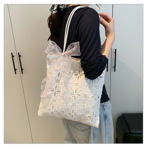 Dettaglio borsa tote in pizzo bianco con nastro floreale e tracolla sulla modella