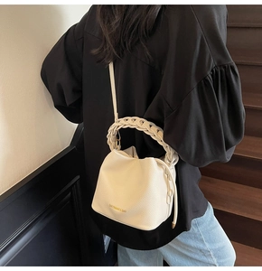Detail of off-white lychee grain leather bucket bag with woven handle and gold lettering